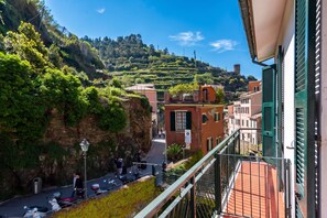 A balcony with a view of a hillside, a street with parked scooters, and buildings with traditional architecture.