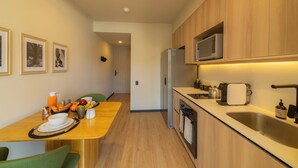 A modern kitchen with wooden cabinets, a stainless steel sink, and a microwave. There is a dining table with chairs and a breakfast setup. - Beautiful Studio (Santa Ana)