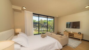 A modern bedroom with a large bed, a sofa, a TV, and a view of greenery outside. - Beautiful Studio (Santa Ana)