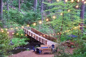 A wooden bridge over a stream in a forested area with string lights.