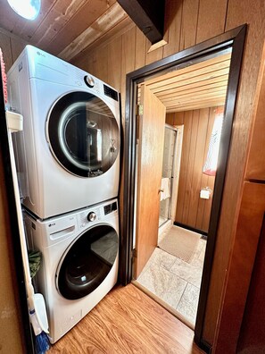 A laundry room with stacked washers and dryers, wooden walls, and a door leading to another room. - Creekside Cabin+Fire Pit+Lakes Nearby+Wine Tasting+Bear Valley Ski Resort (Arnold)