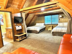 Un dormitorio acogedor en el ático con dos camas, un televisor y un escritorio pequeño.