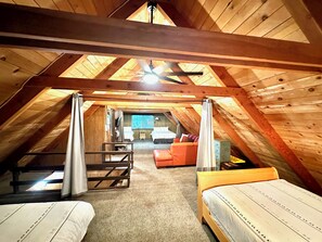 Ein Schlafzimmer im Dachgeschoss mit schrägem Dach, einem Bett, einem kleinen Sofa und einem Fenster mit Jalousien.