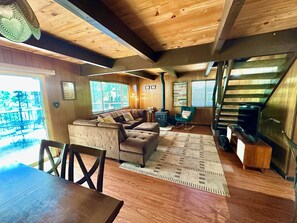 L’intérieur d’un chalet accueillant, avec un plafond en bois, un ensemble de canapés, un fauteuil à bascule, une cheminée et un escalier.