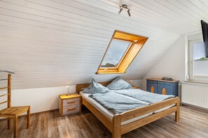 A bedroom with a sloped ceiling, a skylight, a wooden bed, a nightstand, a chair, and a dresser.