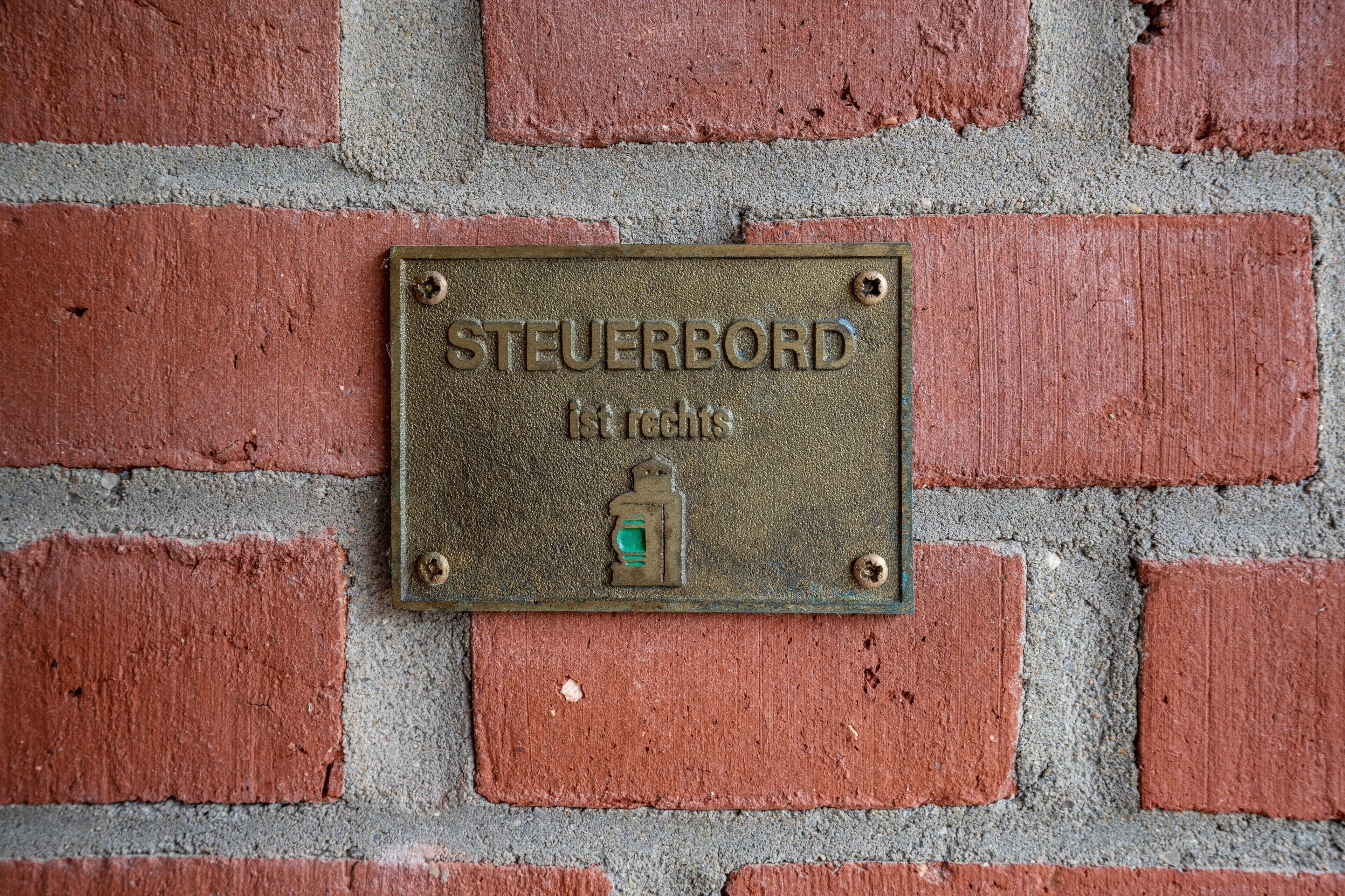 Una placa metálica con la inscripción 'STEUERBORD 1st rights' montada en una pared de ladrillo.
