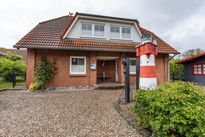 A brick house with a red and white lighthouse, gravel driveway, and a small porch.
