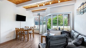 Una sala de estar moderna con techo de madera, un televisor de pantalla plana, un comedor con sillas y una mesa, y un sofá de cuero.