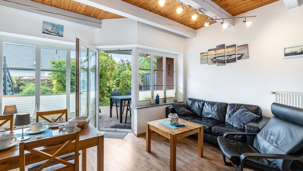 Una sala moderna con techo de madera, un sofá de cuero negro, una mesa de comedor de madera y vistas amplias a través de grandes ventanales.