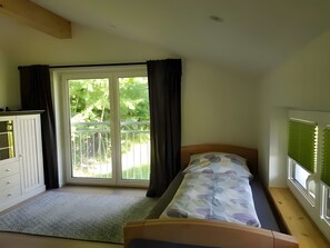 Un dormitorio con cama, armario, ventana con cortinas y vistas a zonas verdes.