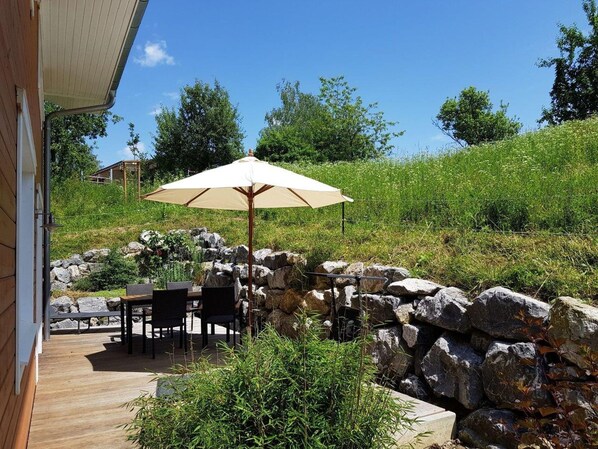 Un patio al aire libre con una mesa, sillas, un paraguas grande y un muro de piedra.