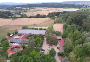 An aerial view of a rural property with fields, a building with solar panels, and a red-roofed structure.