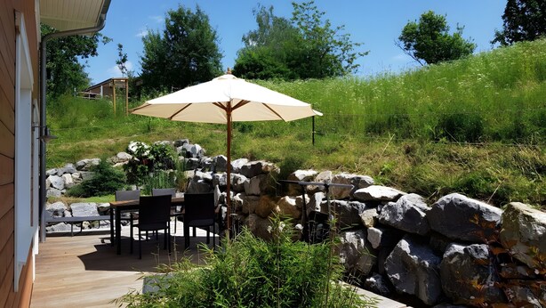 An outdoor patio with a table and chairs, a large umbrella, and a stone wall. - Holiday Home 'Sonnenweide, 85qm' with Private Terrace, Shared Garden and Wi-Fi (Salem)