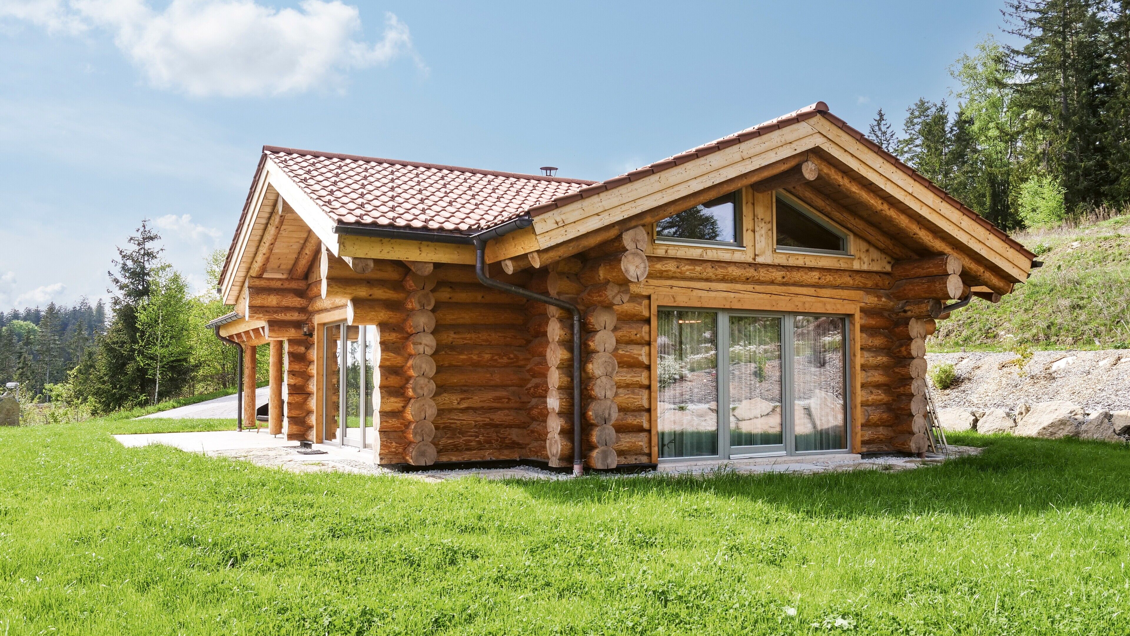 A log cabin with a sloped roof, large windows, and a grassy yard.