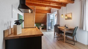 Eine moderne Küche mit Holzbalken, einer schwarzen Dunstabzugshaube und einem Essbereich mit einem Holztisch und Stühlen.