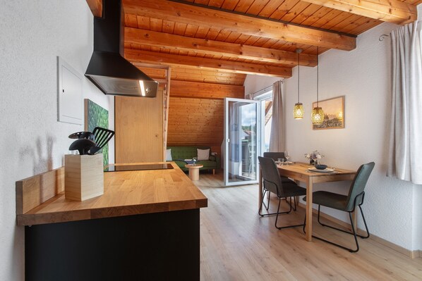 A modern kitchen with wooden beams, a black range hood, and a dining area with a wooden table and chairs.