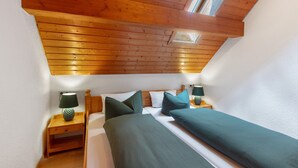 Ein Schlafzimmer mit geneigter Decke, Holzbalken, einem Oberlicht, zwei Nachttischen mit Lampen und einem Bett mit grüner Bettwäsche.