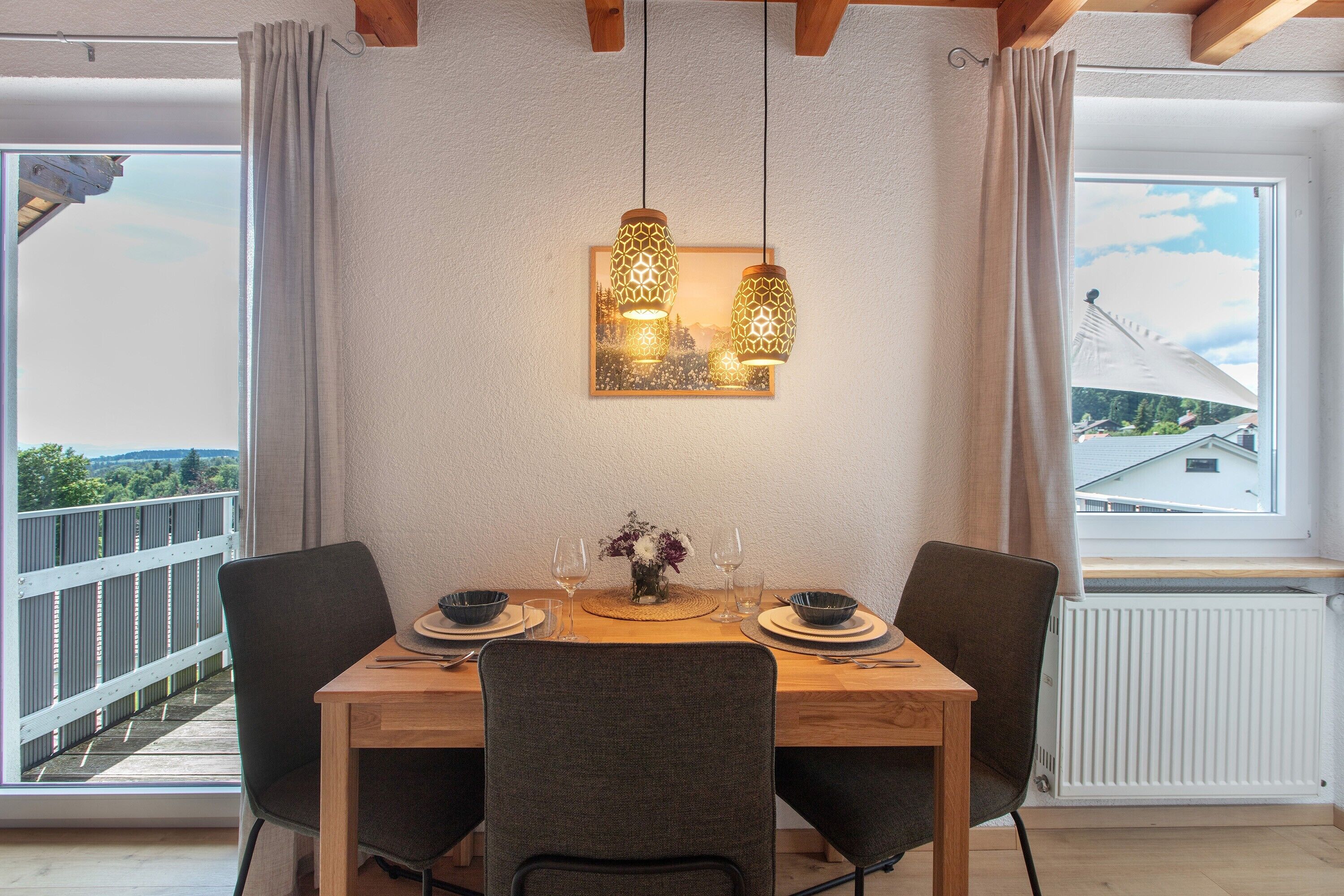 Een eethoek met een houten tafel, twee stoelen, een bloemenvaas en hangende hanglampen.