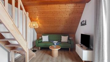 A wooden staircase, a green sofa, a coffee table, a TV on a white stand, and a wall with a forest mural.