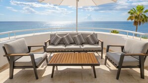 Une terrasse avec un canapé, deux fauteuils, une table et un grand parasol.