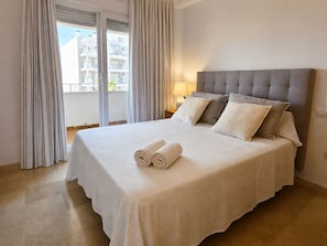 A hotel room with a large bed, curtains, a nightstand, and a view of buildings.