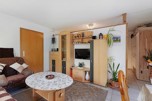 Un espace de vie compact comprenant un canapé, une table ronde, un téléviseur, des meubles en bois et une plante en pot.