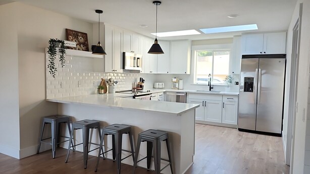 A modern kitchen with white cabinets, a central island with bar stools, a stainless steel refrigerator, and pendant lighting. - Sandy Pacific Hideaway-hot tub, smart tv, woodstove. 4 bedroom home. Florence,OR (Florence)