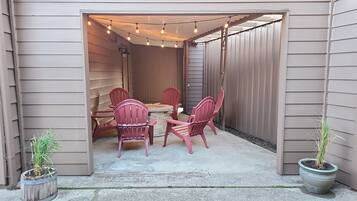 Eine Terrasss mit rundem Tisch, vier Stühlen, Lichterketten darüber und zwei Kübelpflanzen.