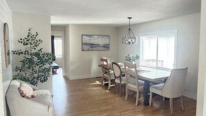 A spacious dining area with a wooden floor, white walls, and a large window. - Sandy Pacific Hideaway-hot tub, smart tv, woodstove. 4 bedroom home. Florence,OR (Florence)