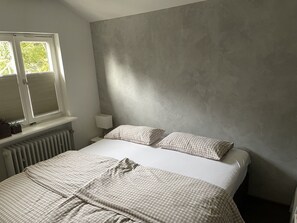 A bedroom with a bed, a window with blinds, a bedside lamp, and a radiator.