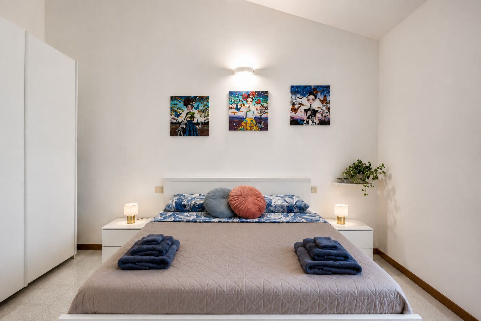 Un dormitorio con una cama, dos mesitas de noche y tres obras de arte colgadas en la pared.