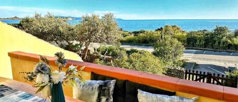 A balcony with a view of the sea, a vase with flowers, and a railing.