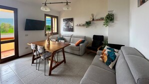 Ein Wohnzimmer mit Esstisch, Sofa und einem an der Wand montierten Fernseher.