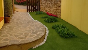 Ein angelegter Garten mit einem gepflasterten Weg, einem Holztor und einer gelben Mauer.