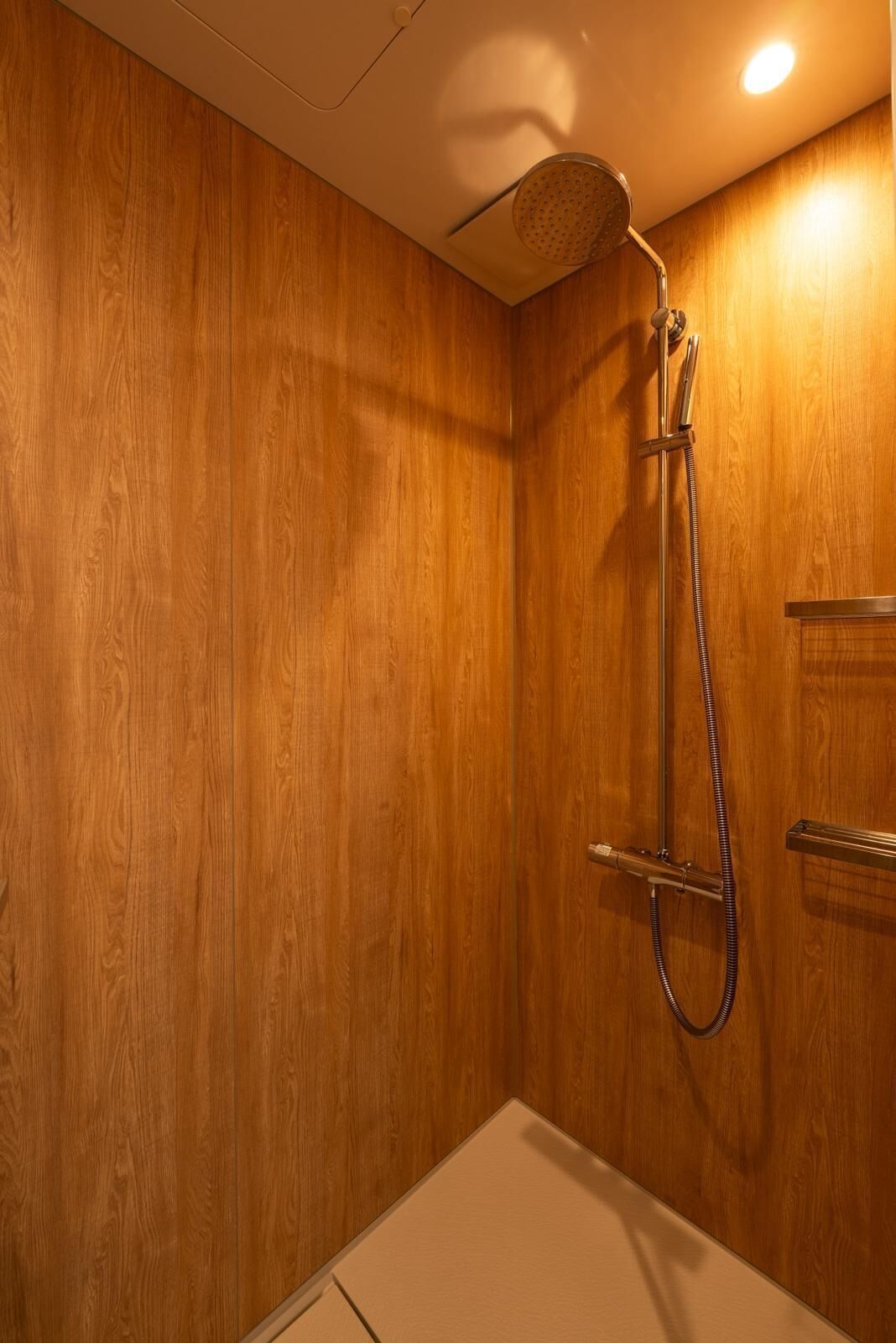 Une salle de bain aux murs lambrissés, équipée d’une douche, d’un porte-serviettes et de toilettes.