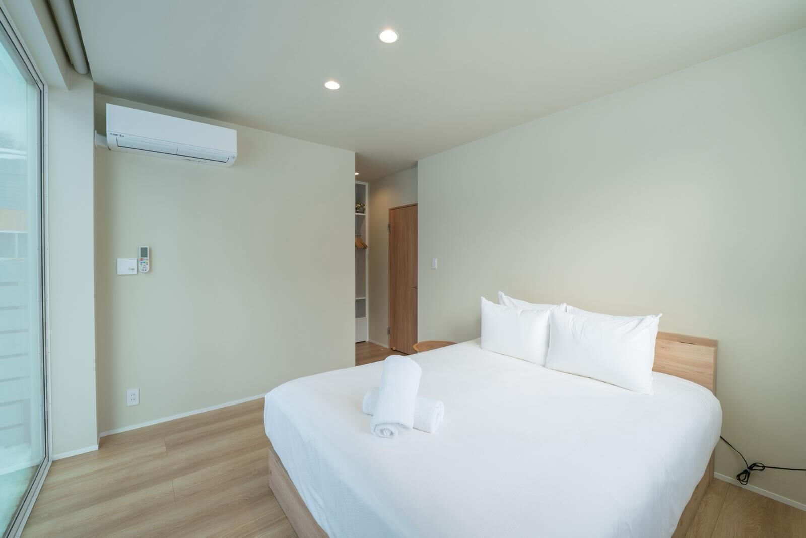 A hotel room with a bed, an air conditioning unit, a control panel, and a view through a window.