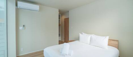 A hotel room with a bed, an air conditioning unit, a control panel, and a view through a window.