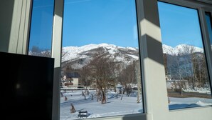 Uitzicht door grote ramen op een besneeerd landschap met bergen, een weg en gebouwen.