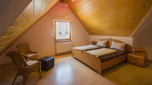 Une chambre avec un plafond en pente, un lit, une table de chevet, une chaise et une fenêtre.