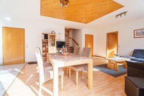 Uma sala de estar moderna com uma mesa de jantar de madeira, cadeiras, um sofá e uma televisão.