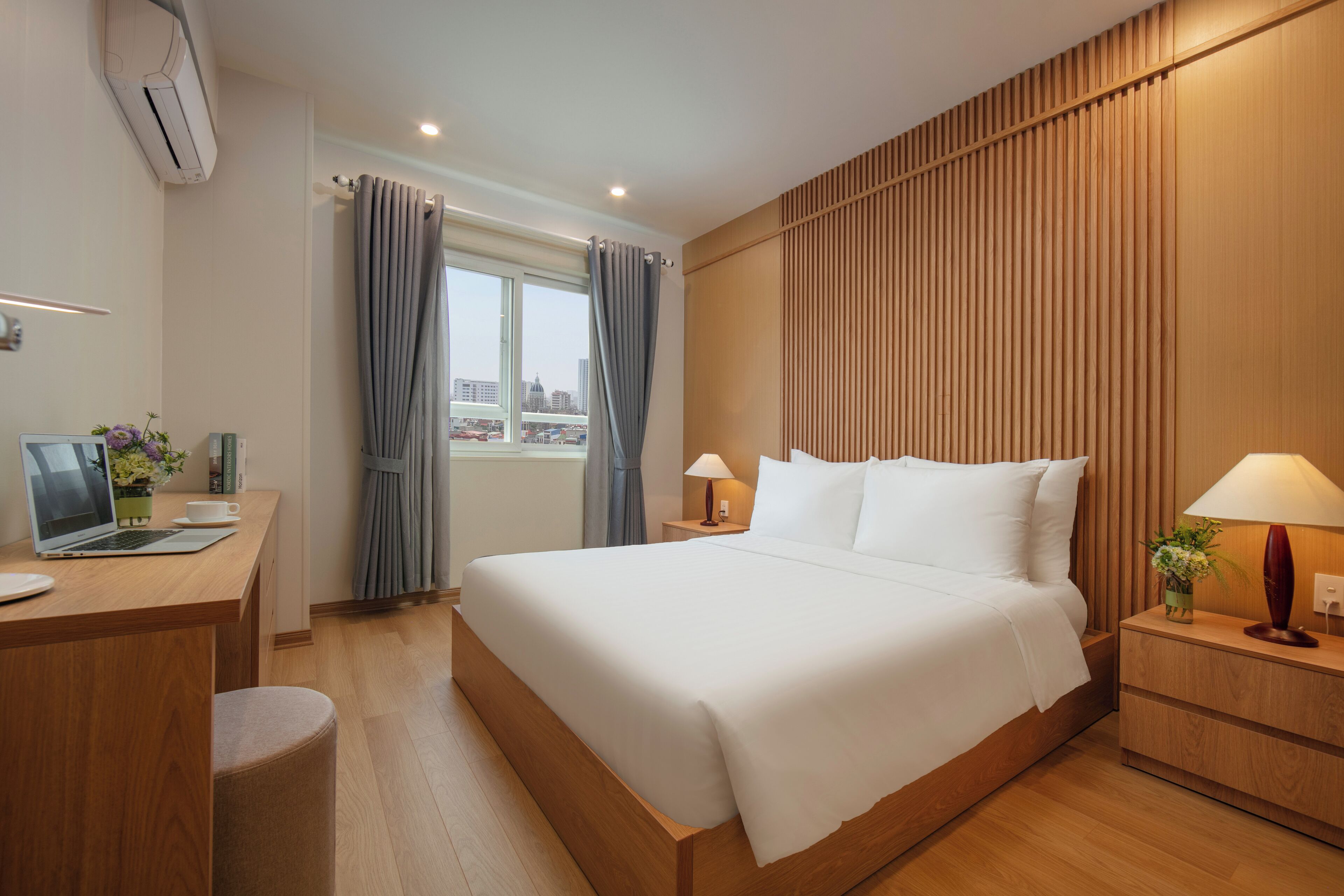Une chambre d’hôtel avec un grand lit, un bureau avec un ordinateur portable, une table de chevet avec une lampe et une fenêtre avec des rideaux.