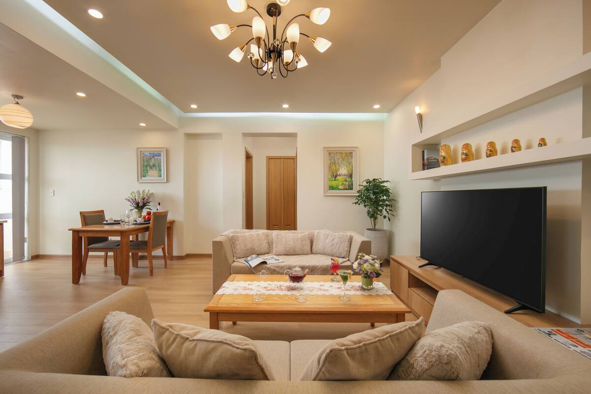 A modern living room with a sofa, coffee table, TV, and dining area.