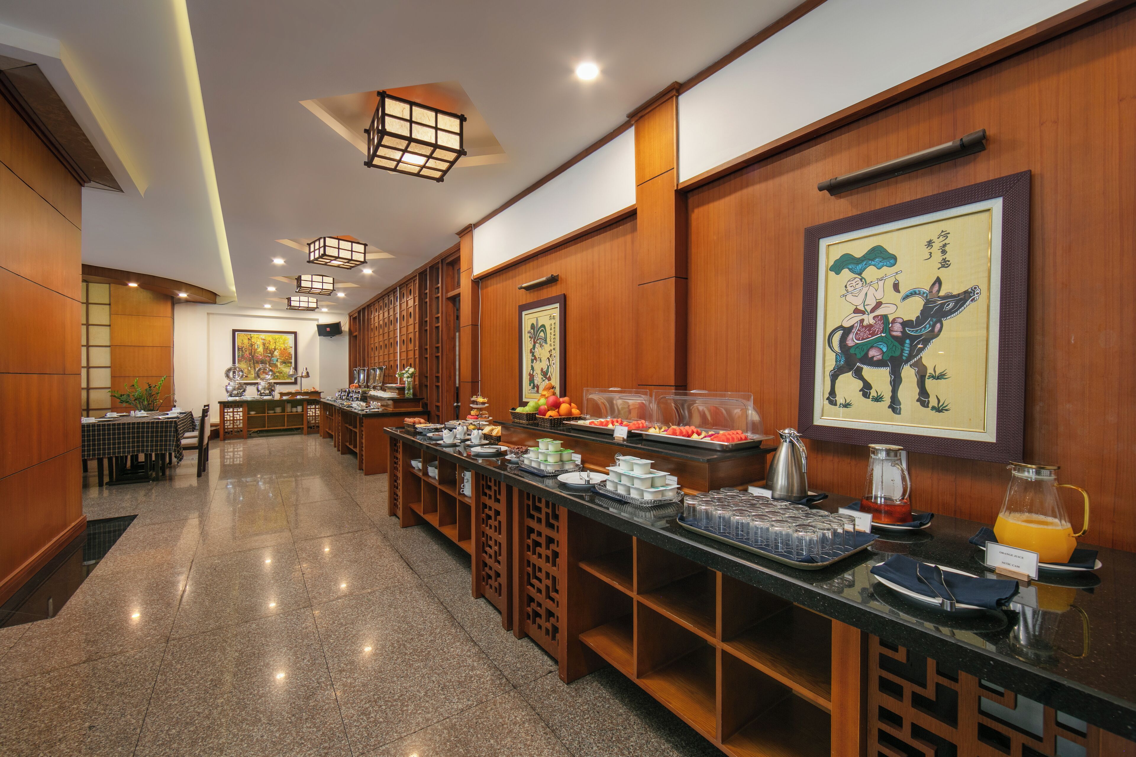 A hotel breakfast area with a buffet setup, wooden paneling, and traditional artwork.