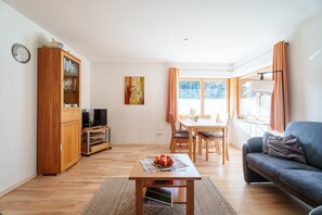 Uma sala de estar com sofá, mesa de jantar, televisão e armário.