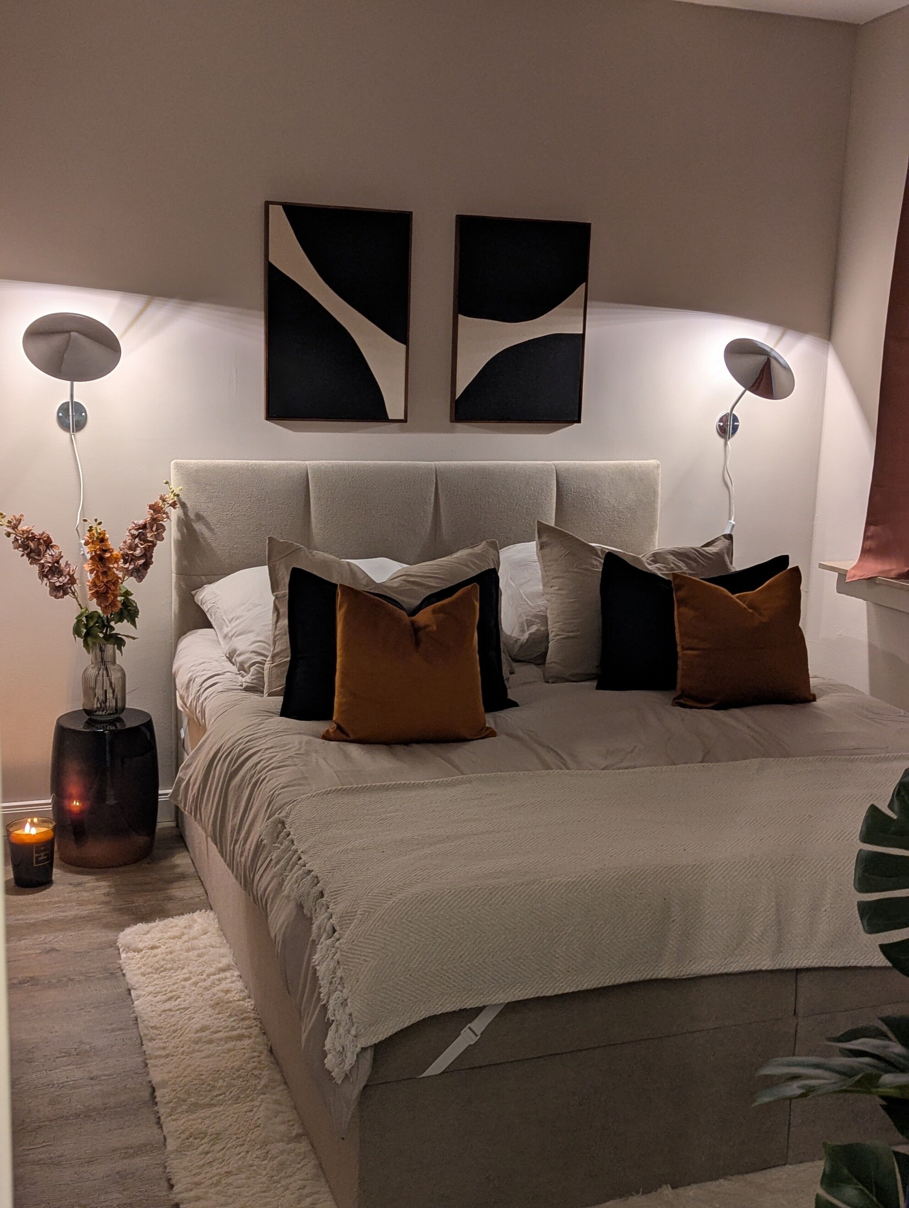 Un lit avec une tête de lit, des lampes de chevet, un vase avec des fleurs et une bougie sur une table de chevet.