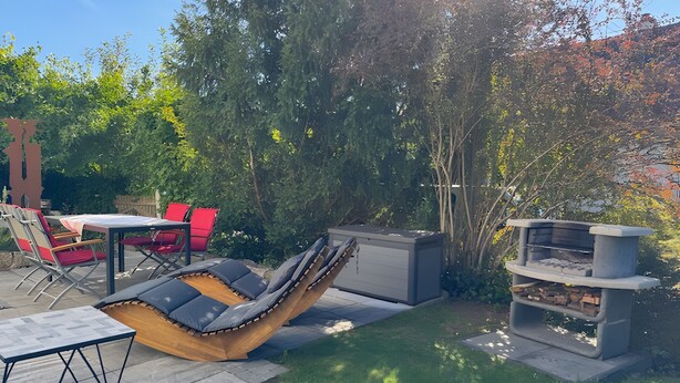 A patio with a lounge chair, a table, red chairs, and a built-in barbecue grill.