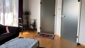 Una habitación con un sofá, una mesita, una silla, una lámpara, una puerta y una alfombra.