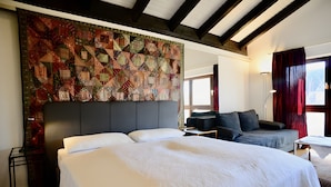 Habitación de hotel con una cama grande, un sofá, un escritorio y un tapiz decorativo en la pared.