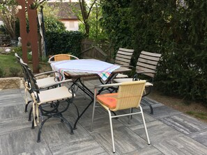 An outdoor patio with a table and chairs, surrounded by greenery and a wooden fence. - Apartment 'Peperoni' with Private Garden and Wi-Fi (Moos)