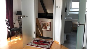 Una habitación con piso de madera, un tapete rojo y blanco, un escritorio con una lámpara y una silla.
